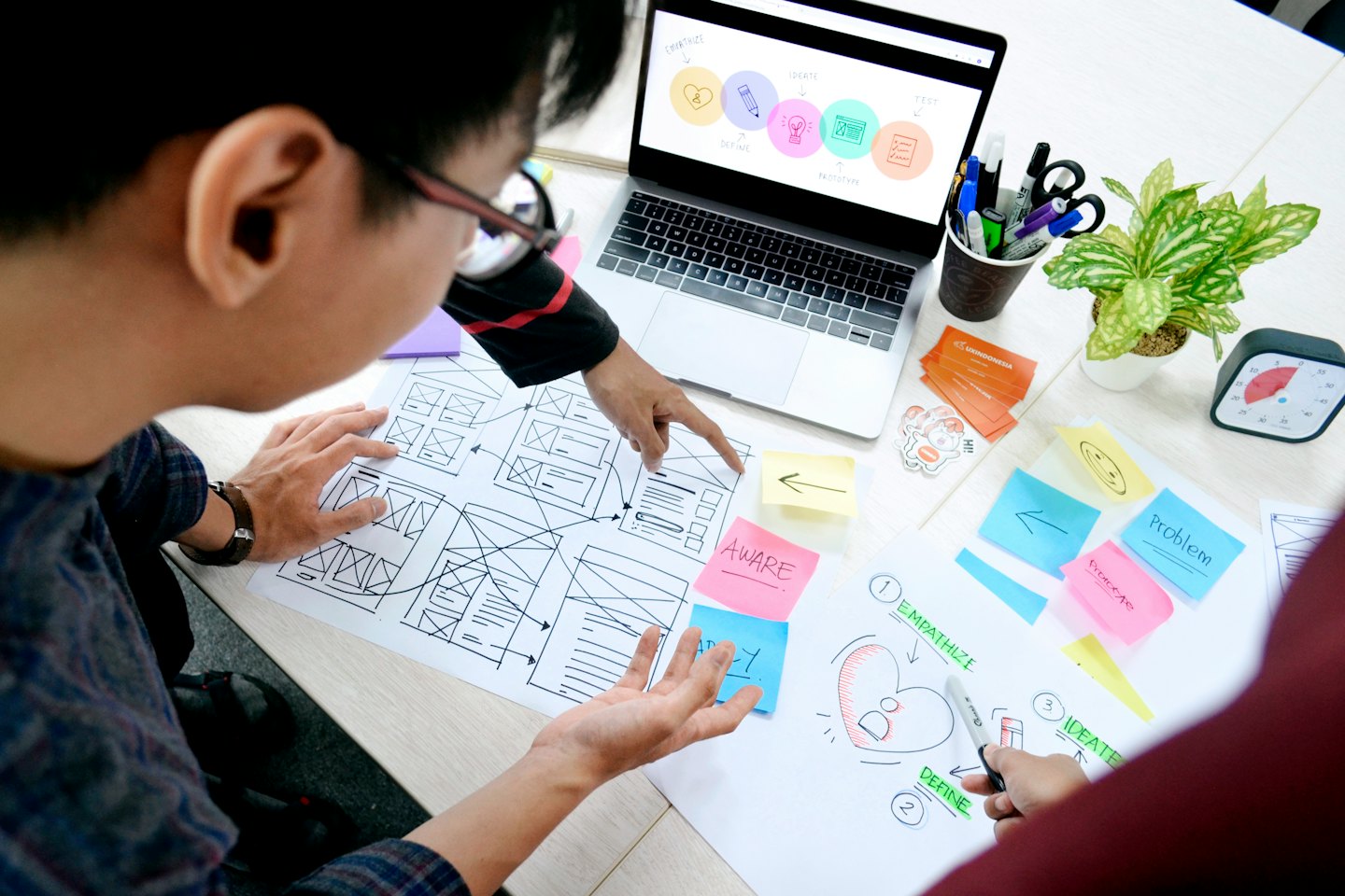 Two men collaborating on UX/UI design project with wireframes and sticky notes.