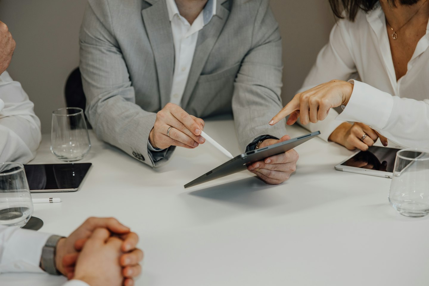 Business professionals collaborating on a tablet at a white table.